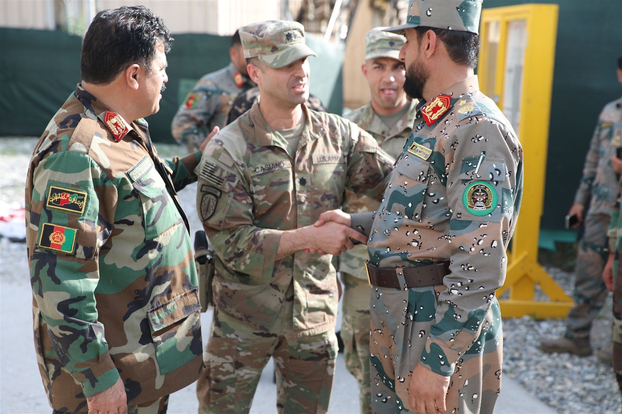 A U.S. Army advisor shakes hands with an Afghan military officer as other soldiers look on at a base in Afghanistan.